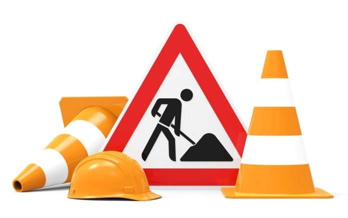 cartello triangolare con bordo rosso che raffigura un operaio al lavoro con una pala, inoltre si vedono due coni stradali bianchi e arancioni. Nel complesso, l’immagine comunica il tema di cantieri stradali di lavori in corso.